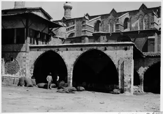 Two men standing beside sacks under the arcade of a stone building in Nicosia