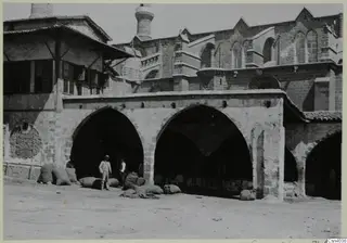 Two men and several sacks beside an arcaded stone building in Nicosia