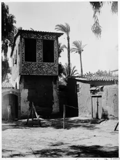 Upper wooden storey with lattice-patterned panels on a mud-brick building, with palm trees, in Nicosia