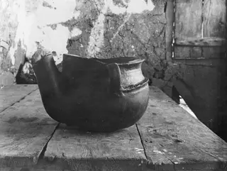 Round-bodied clay pot with a broken rim, standing on a wooden table at Klirou