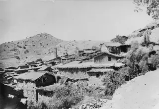Stone houses with tiled and flat roofs climb a hillside village at Lazania, with bare hills behind.