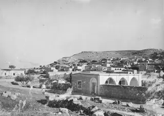 Village houses on a rocky hillside on the Karpas peninsula, with a man walking on a path in the foreground.