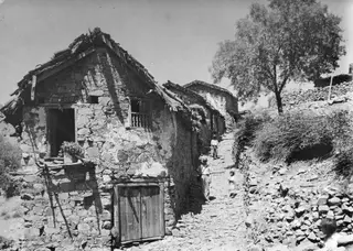 Stone houses and a stone-paved lane in Lazania, with two or three people walking uphill between them.