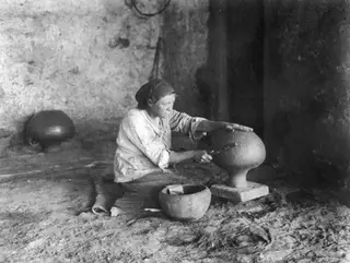 Woman polishing a large pottery vessel while seated on an earthen floor at Klirou