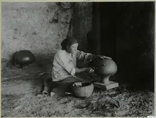 Woman polishing a large footed vessel on a block in a dark interior at Klirou