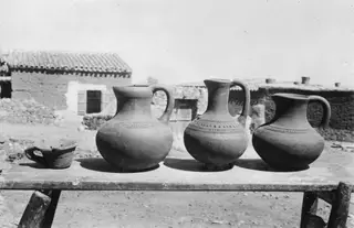 Three handled jugs and a small bowl on a wooden table in front of a farmstead building at Klirou