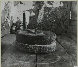 Two grinding stones for grain on a wooden table in front of a cracked plaster wall.
