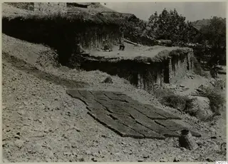 Stone house with a grass-covered roof, rows of drying dark blocks and woven baskets at Lazania