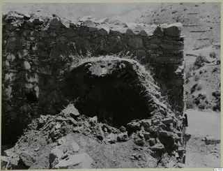 Ruined stone wall with an arched oven opening, its vault partly broken, and fallen rubble in front