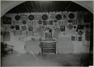 Cottage interior at Milia with embroidered wedding wall hangings, two beds and a carved chest of drawers