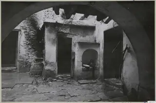 Courtyard of a building seen through a stone arch, with a wall niche holding a jug and a shallow bowl.