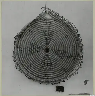 Round coiled straw basket with a concentric spiral pattern, hung on a wall.
