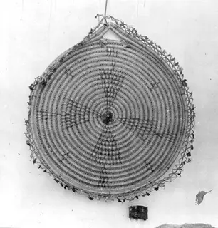 Round coiled Cyprus handicraft with concentric rings, hung by a loop against a pale wall