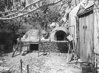 Domed oven with an arched opening in a yard, beside a whitewashed wall with a wooden door