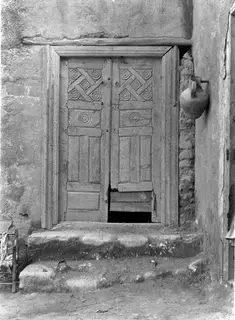Carved wooden double door with rosette and lattice panels set in a plastered wall, with stone steps leading up to it
