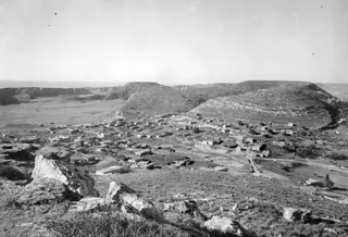 View from a rocky hill over the village of Galinoporni, with low houses in the valley and bare hills beyond.
