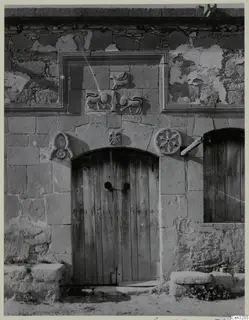 Stone building front with a wooden plank door under an arch, carved relief panels with animals and a bird above
