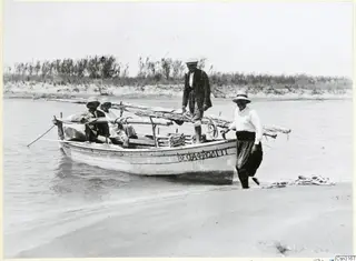 Small wooden boat with four people at the water's edge on a sandy shore
