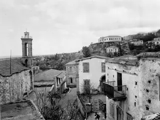 Village street in Lapithos with a stone bell tower, whitewashed houses and a few people by the steps.