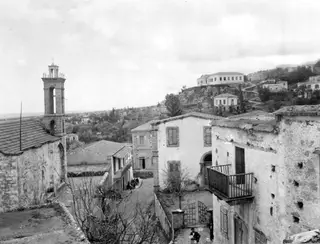 Village street in Lapithos with a stone church bell tower and whitewashed houses with shuttered windows