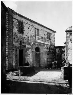 Two-storey stone building with a balcony and arched doorway in Nicosia, with people and a walking stick in the street