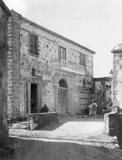 Two-storey stone building with a balustraded balcony and arched doorway, with people and a walking stick in a Nicosia street