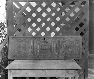 Carved wooden panel with rosettes and a central columned motif, standing on a table in front of a lattice.
