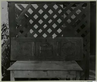 Carved wooden panel with two rosettes and a central arched motif, set above a low wooden box with a flat top