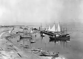 Harbour at Famagusta with sailing boats moored along the quay and a long city wall on the left.