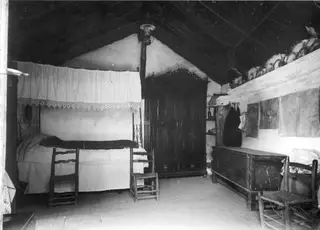 Interior of a room in Lazania with a canopied bed, wooden chairs, a dark wooden cupboard and a chest