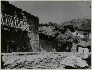 Stone village buildings with a timber balcony, a stone wall and a hillside at Lazanias