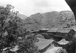 Village of stone houses with tiled roofs on a steep hillside at Lazania, with trees in the foreground.