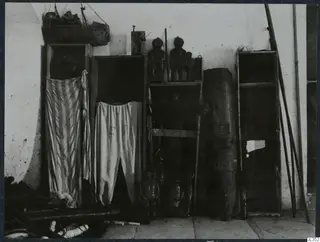 Wooden cupboards and shelves against a whitewashed wall, holding carved wooden figures and striped cloth