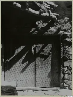 Carved wooden double door with diamond-pattern panels and an iron latch, set in a stone wall at Lazania