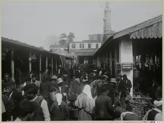 Crowded covered market street in Nicosia, with timber-posted stalls and people in caps, hats and headscarves