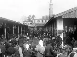 Crowded market street in Nicosia with open-fronted stalls on both sides and a minaret rising behind the rooftops.