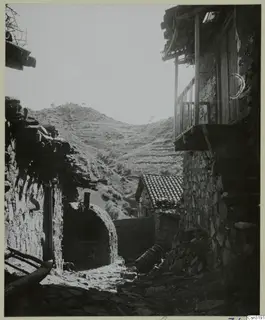 Stone village lane at Lazania with a wooden balcony on a stone house and terraced hills behind