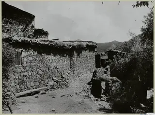 Stone-walled village lane at Lazanias, with tiled roofs and mountains rising behind the houses