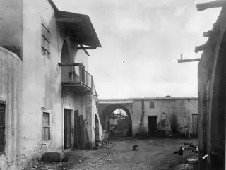 Courtyard of a village house with whitewashed walls, a timber balcony, a ladder and a domed oven