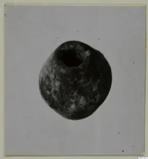 Rounded stone object with a large circular hole at the top, photographed on a pale card.