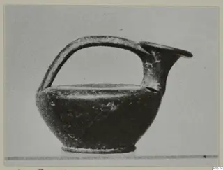 Small black-glazed jug with a strap handle and trefoil-like spout, photographed against a plain grey background.