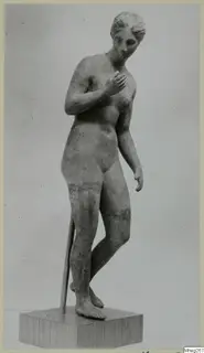 Standing nude statue of a female figure with one hand on her chest, on a wooden plinth
