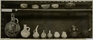 Pots and bowls from Lapithos Markides, T.15A, set out on two wooden shelves against a dark cloth.