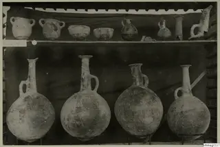 Pots, bowls and jugs displayed on two shelves against a dark cloth, from Lapithos Markides