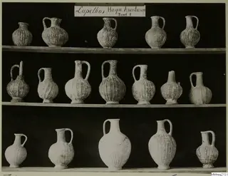 Three shelves of ribbed pottery jugs with single handles, Lapithos Markides T.1, photographed against a black background