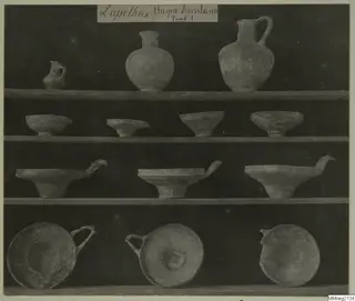 Jugs and bowls from Lapithos Markides, T.1, arranged on four shelves against a dark background
