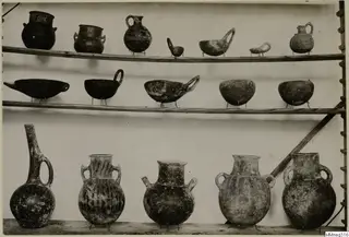 Pottery vessels from Cyprus on three wooden shelves: jugs, jars and bowls, several with geometric decoration.