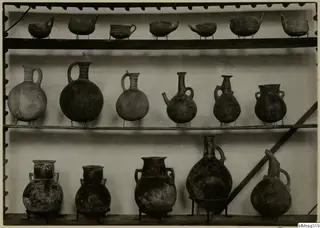Shelves of pottery vessels on wire stands, including jugs, juglets and bowls with painted or incised patterns