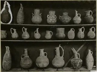 Three shelves of painted pottery jugs and jars, pattern-decorated, shown against a dark cloth at the Cyprus Museum.