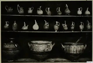 Three shelves of painted pottery jugs and jars, photographed against a dark background in a museum display.